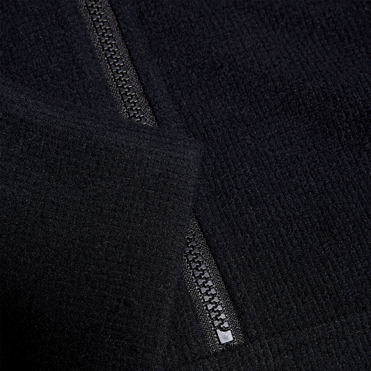 Black fabric with a textured surface features a visible zipper partially open at the edge suggesting an outerwear garment in a neutral background that highlights the material's softness and detail.