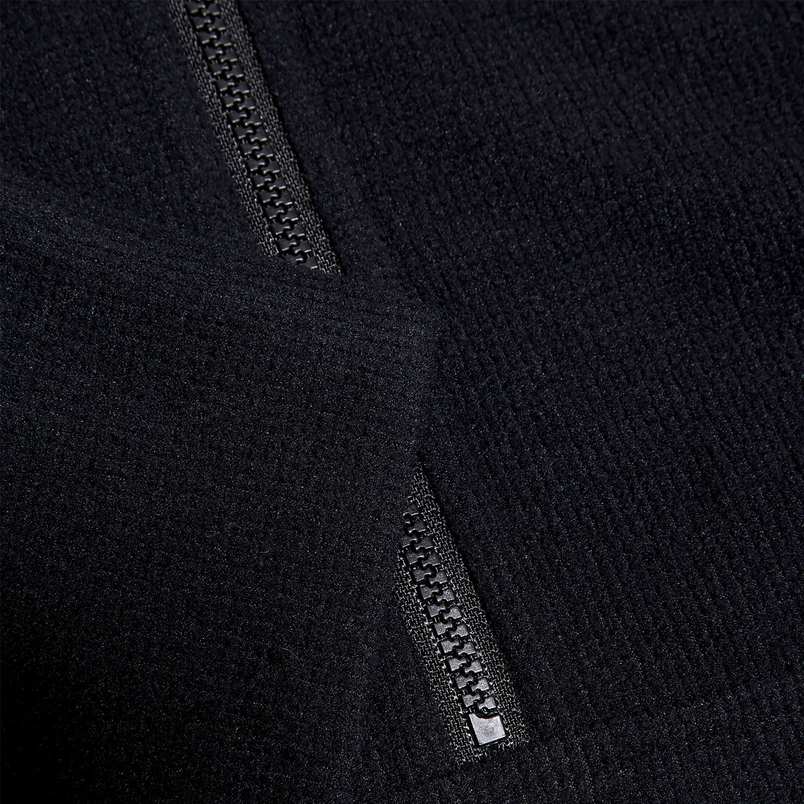 Black fabric with a textured surface features a visible zipper partially open at the edge suggesting an outerwear garment in a neutral background that highlights the material's softness and detail.