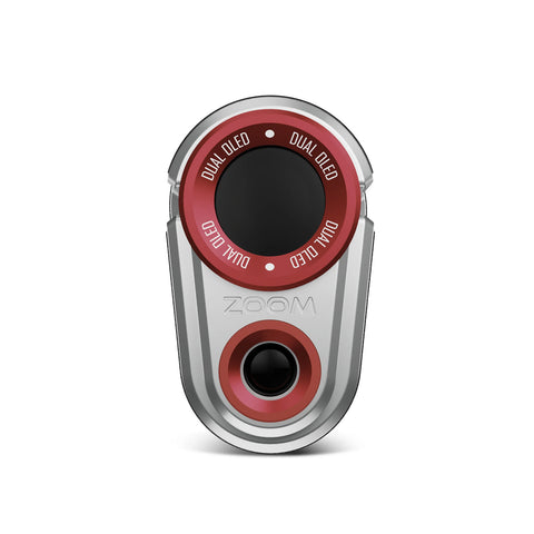 A compact electronic device with a metallic silver body features a circular red dial labeled "DUAL OLED" and a small black lens at the bottom center for audiovisual functionality.