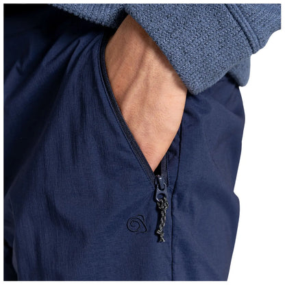 A hand is positioned inside a zippered pocket of dark blue pants while wearing a gray textured sweater showcasing a casual outfit.