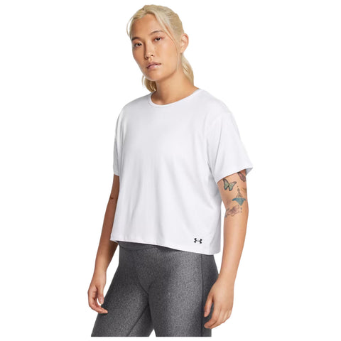 A person stands confidently wearing a white t-shirt and gray leggings showcasing visible tattoos on their arms with a neutral background emphasizing their casual athletic attire.