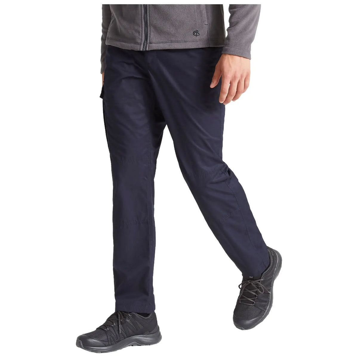 A person is walking in dark blue pants and black shoes. They wear a gray zip-up jacket, and the focus is on their lower body as they move forward in a neutral space.