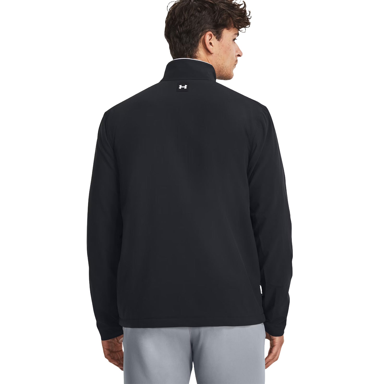 A man wearing a black jacket stands facing away with his head turned slightly to the right showing a collar and a logo on the back in a neutral bac