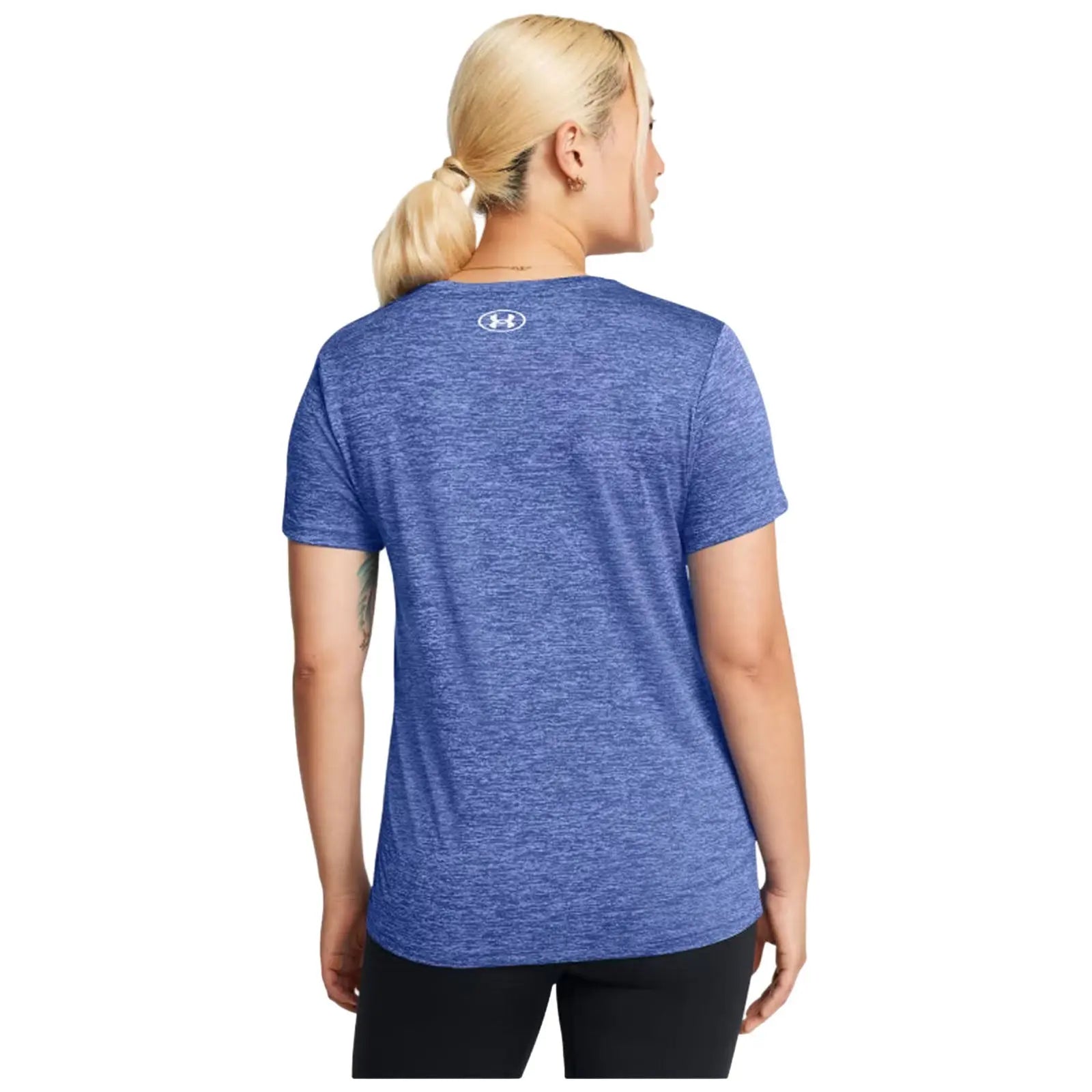 A person with blonde hair in a ponytail wears a blue athletic shirt facing away, demonstrating sportswear in a neutral setting, emphasizing a casual fitness context.