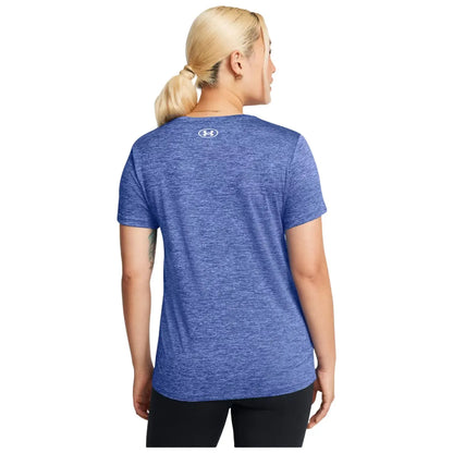 A person with blonde hair in a ponytail wears a blue athletic shirt facing away, demonstrating sportswear in a neutral setting, emphasizing a casual fitness context.