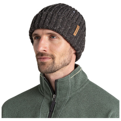 A man with a short beard is wearing a dark knitted beanie and a green zip-up jacket. He is looking slightly to his right, with a neutral expression in a well-lit setting.