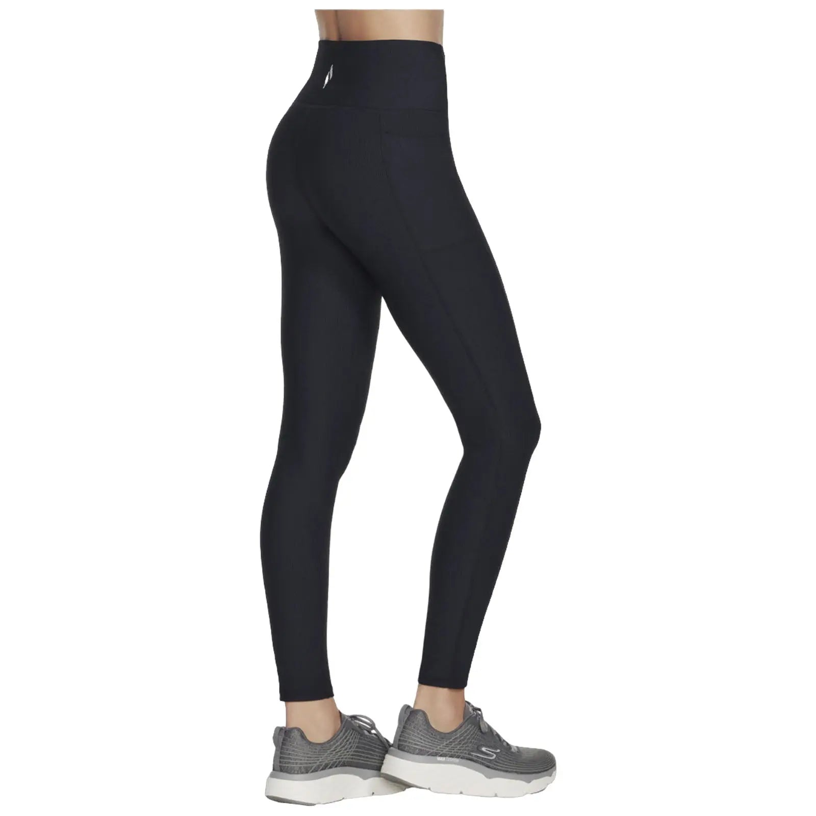 Black leggings with a high waistband are being worn by a person standing sideways. They are paired with grey athletic shoes. The setting is neutral without visible background details.