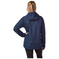 A woman stands with her back facing the viewer wearing a navy waterproof jacket and black leggings with one hand on her hip in a neutral background.