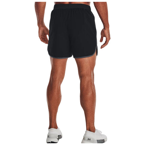 A man stands facing away wearing black athletic shorts and white sneakers his muscular legs are visible in a neutral background showcasing his athletic build and readiness for activity