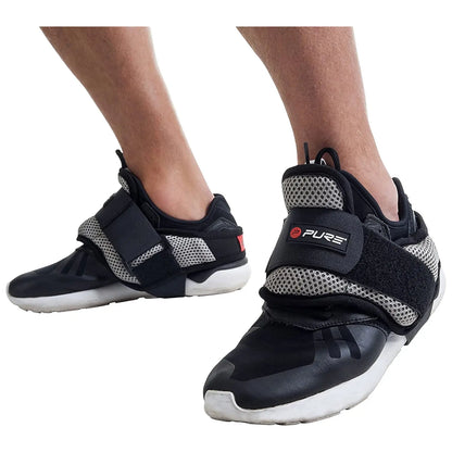 Black and gray athletic shoes with mesh detailing are worn on human feet the shoes feature a wide strap and are situated against a light background