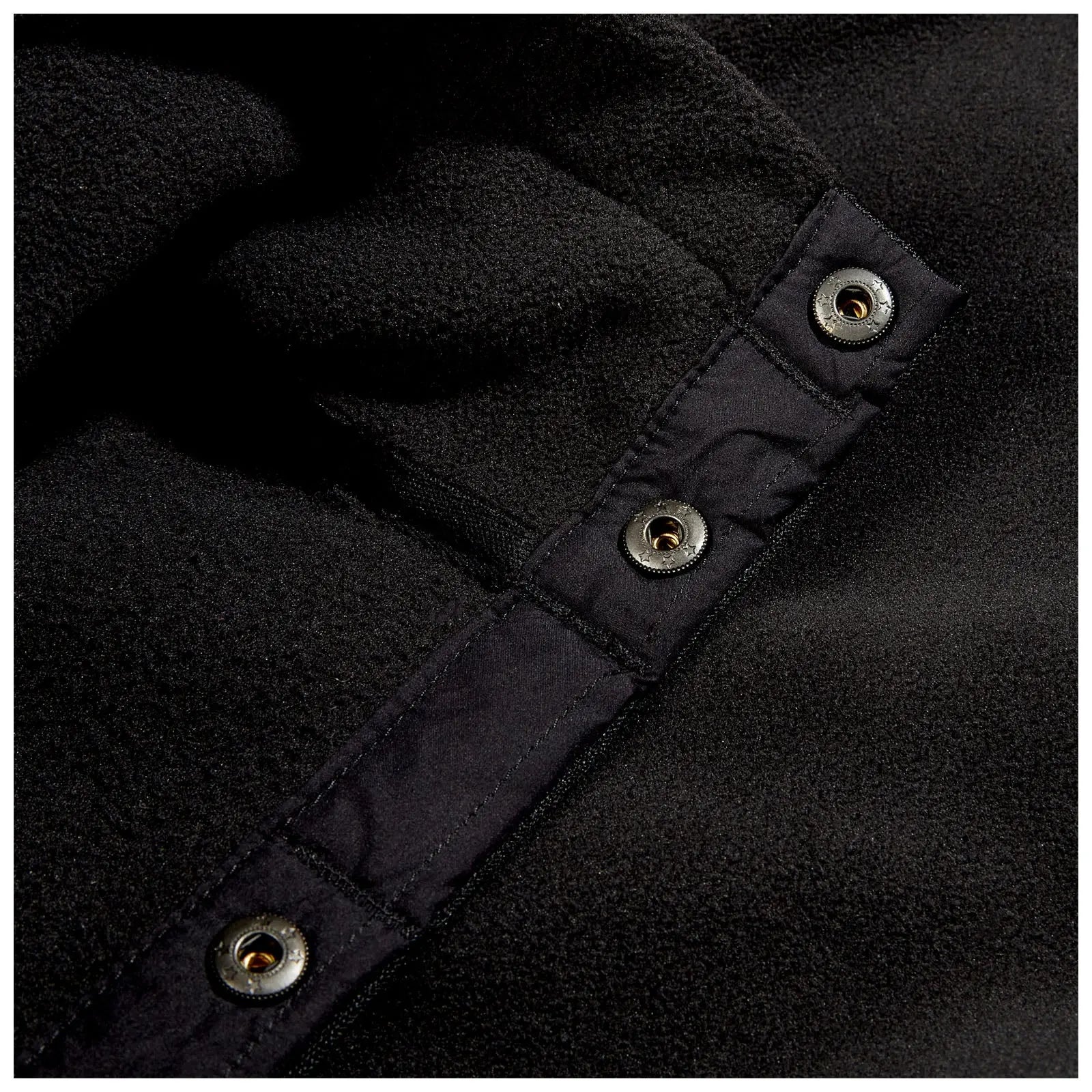 A close-up of a black fleece fabric featuring a button closure with metallic snaps the material appears soft and has a textured surface against a dark background.