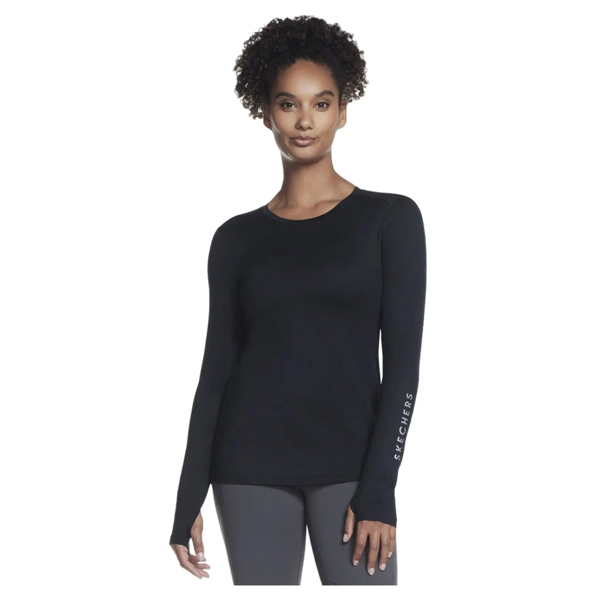 A person stands wearing a black long-sleeve shirt and leggings with the brand name on the sleeve, set against a plain white background, conveying a casual athletic style.