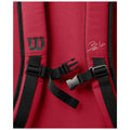 A red backpack is displayed with adjustable straps secured by a black buckle showing a logo and a signature on the surface highlighting a sporty design.