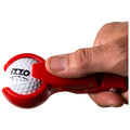 A hand grips a red golf ball cleaner tool as it presses against a white golf ball displaying the logo "IZZO GOLF" in a bright, uncluttered setting.
