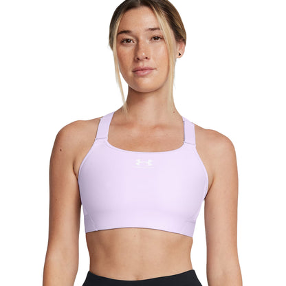A person is wearing a light purple sports bra and black athletic pants while standing upright against a plain background. Their expression is neutral and they have shoulder-length hair.