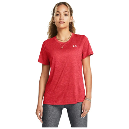A woman stands confidently wearing a red athletic shirt and gray leggings showcasing a casual athletic style in a neutral background.