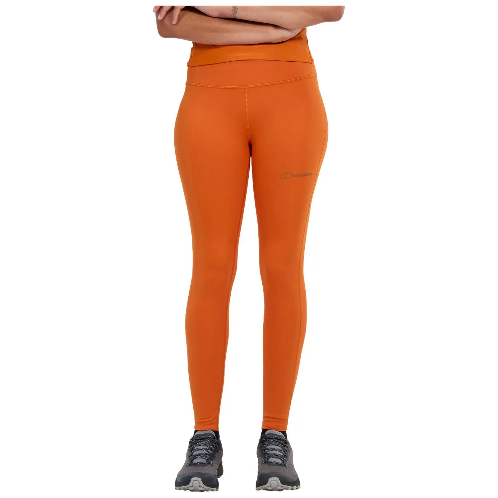 A person is joyfully lifting one leg while standing on the other foot wearing a knotted white shirt and black leggings in a simple white background.