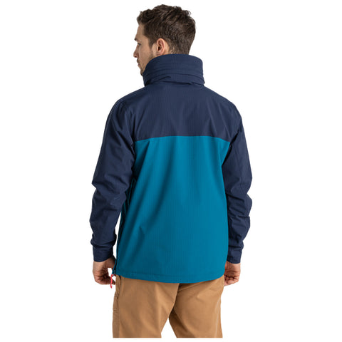 A person is standing with their back facing the viewer wearing a two-tone jacket that is predominantly navy blue on the top and teal on the bottom in a neutral environment.