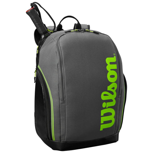 A gray backpack with bright green accents and the brand name Wilson prominently displayed is shown standing upright with a tennis racket partially inserted into the top.
