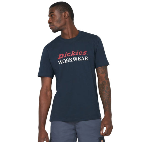 A man stands confidently in a navy blue t-shirt featuring the text Dickies WORKWEAR prominently displayed on the front showcasing a stylish workwear aesthetic.