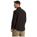 A man is standing with his back turned wearing a black long-sleeve shirt and light khaki pants in a plain white background. His head is slightly turned to the side.