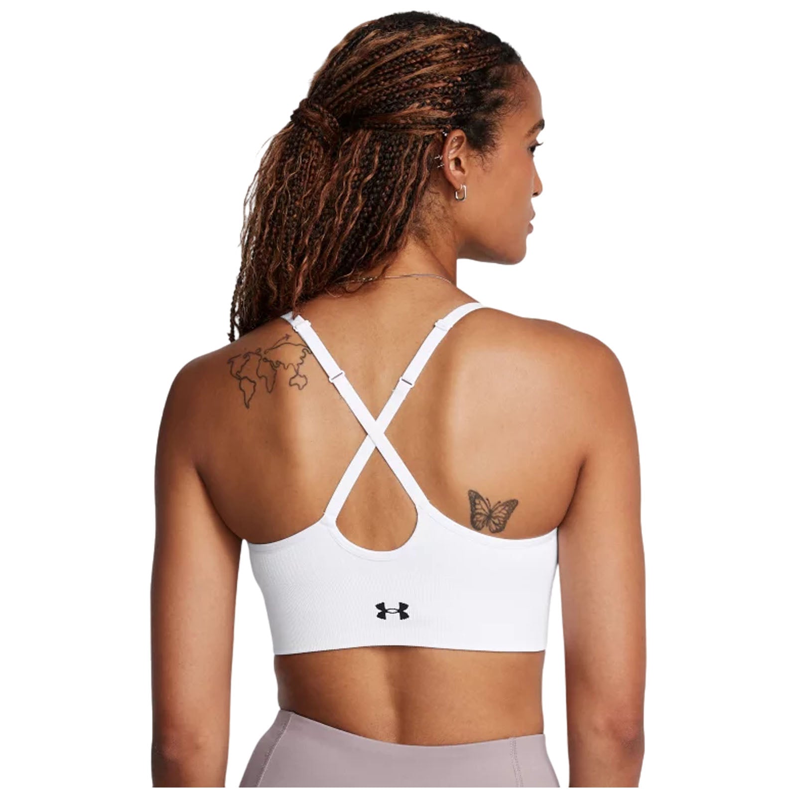 A person is wearing a white sports bra with crisscross straps showcasing a butterfly tattoo on their back in a neutral setting.