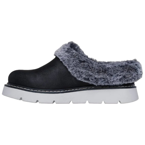A black slipper with a plush gray fur collar rests on a white background featuring a thick gray sole and white stitching along the edge providing a cozy appearance.