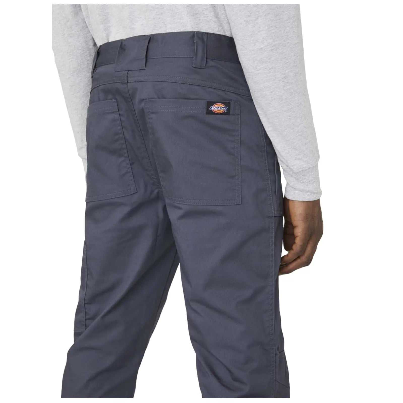 A person stands wearing gray long sleeves and dark gray pants with two back pockets showcasing a label on the waistband the setting is neutral and focused on the clothing details.