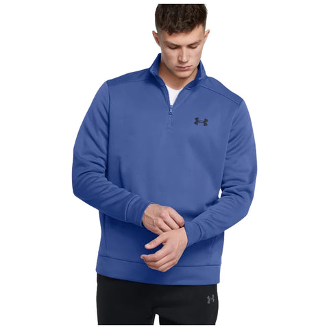 A young man is buttoning a blue pullover sweatshirt with a half-zip closure in a plain background, showcasing a casual athletic look and a logo on the chest