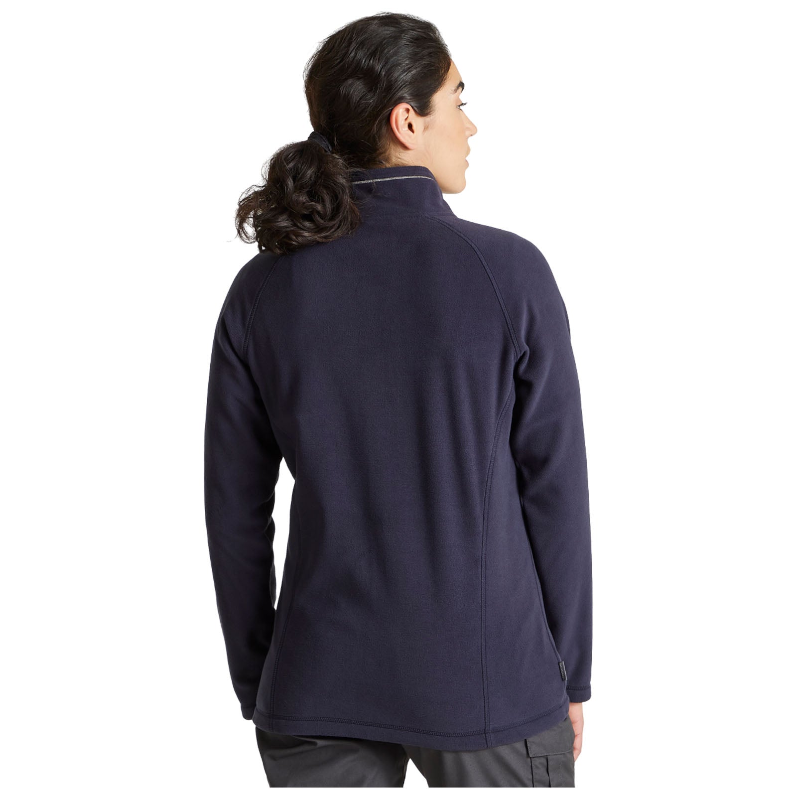 A woman stands with her back to the viewer wearing a navy fleece jacket in a casual setting emphasizing comfort and warmth in a relaxed outdoor or indoor environment