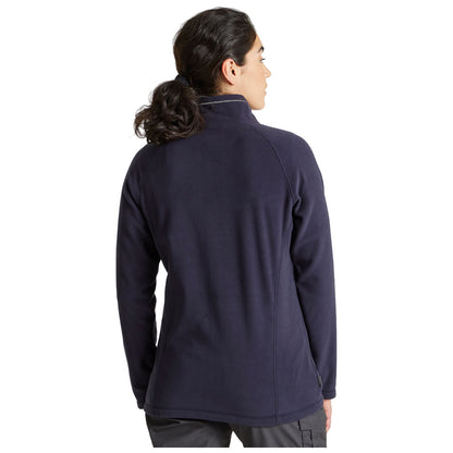 A woman stands with her back to the viewer wearing a navy fleece jacket in a casual setting emphasizing comfort and warmth in a relaxed outdoor or indoor environment
