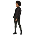 A person stands in a black padded jacket with the front unzipped wearing dark leggings and black boots in a neutral space that highlights their outfit and posture.
