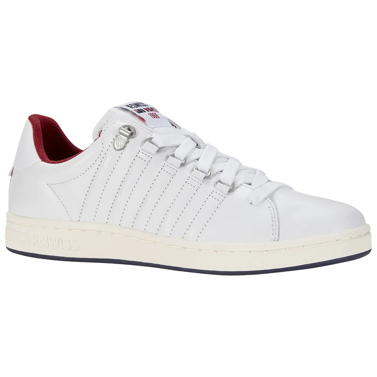 A white sneaker with a smooth leather surface features multiple eyelets for laces and a red interior. It rests on a light-colored sole in a simple, clean design.