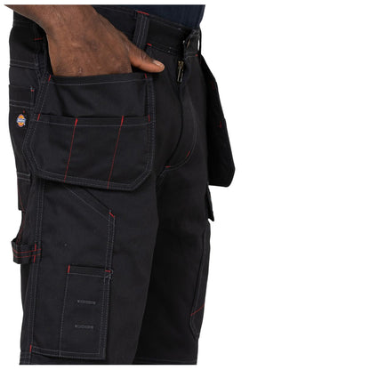 A pair of black cargo shorts features multiple pockets and red stitching The hand rests in one of the side pockets showcasing the garment's utility in a casual setting