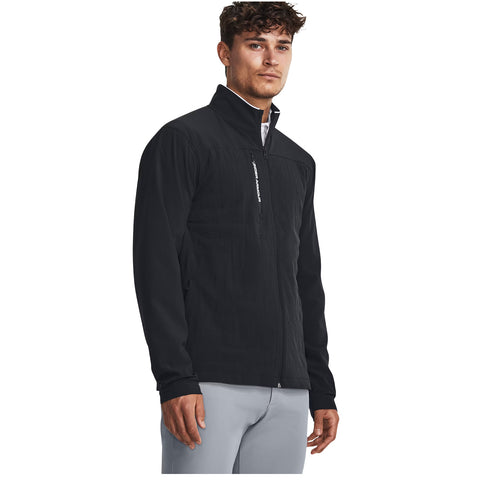 A young man stands confidently wearing a black jacket with a zippered front and high collar complementing light gray pants in a neutral background, showcasing a casual yet stylish outfit.