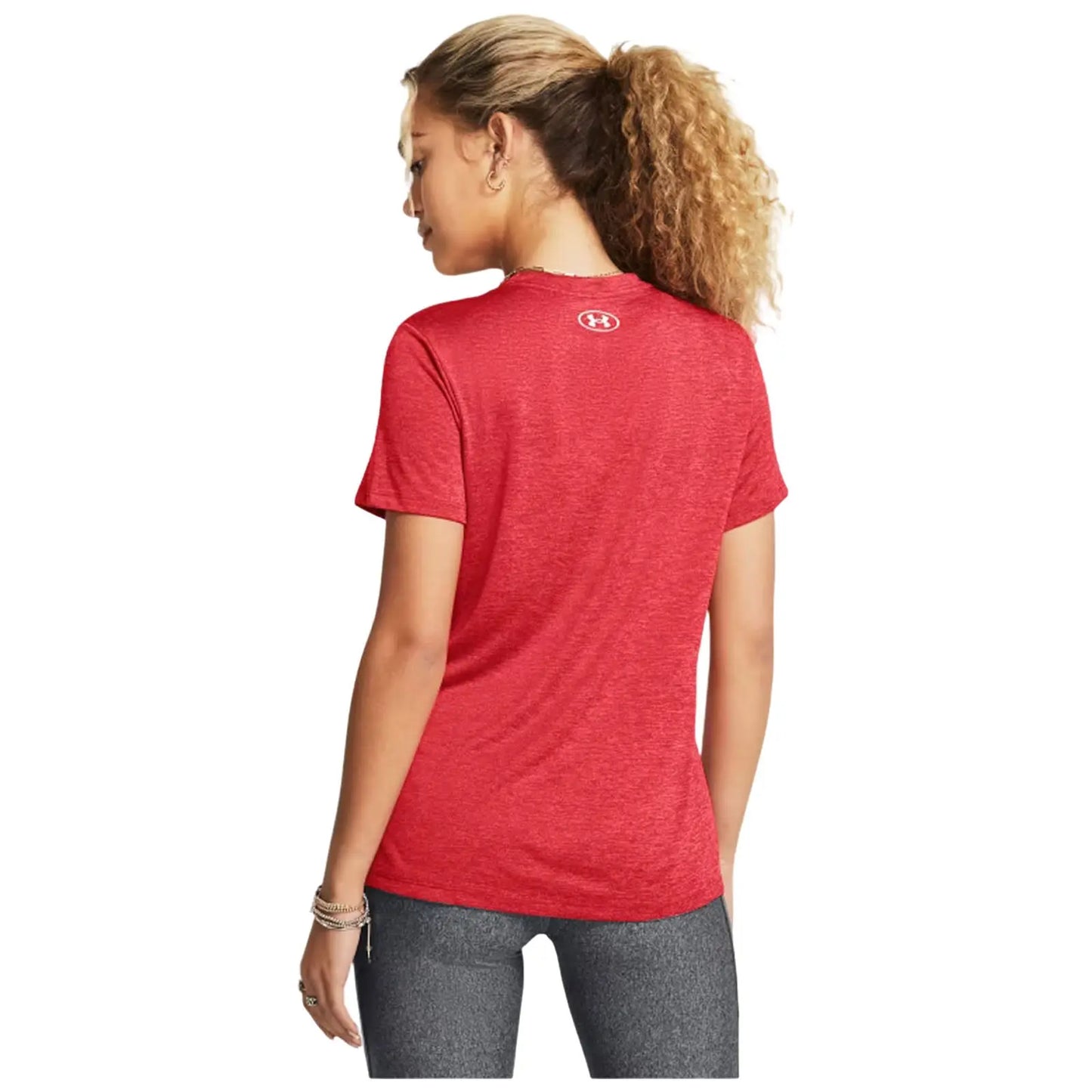 A woman with curly hair is wearing a red athletic t-shirt and dark leggings while standing with her back to the viewer in a plain background.