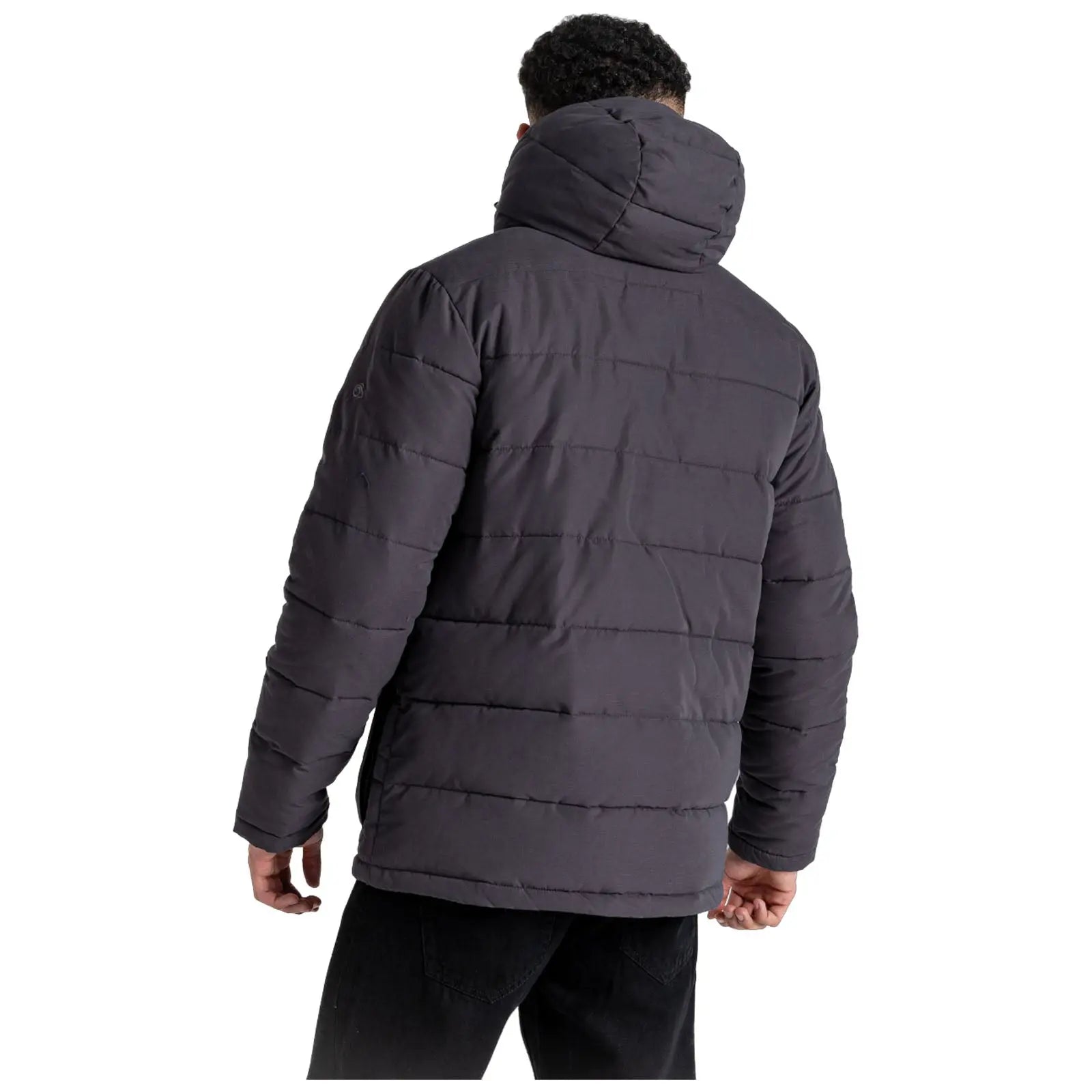 A person wearing a dark puffer jacket stands with their back facing the viewer, hands relaxed by their sides against a plain white background.
