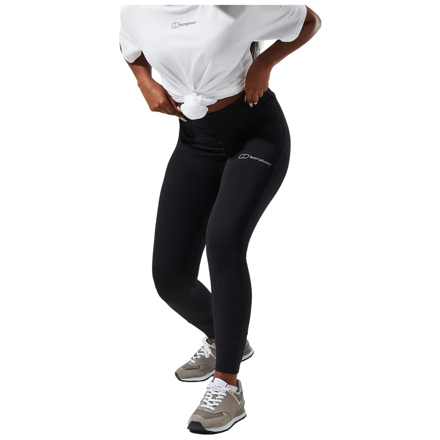 A person is wearing olive green leggings featuring a logo on the lower leg while standing with one hand resting on the hip and the other hand at their side.