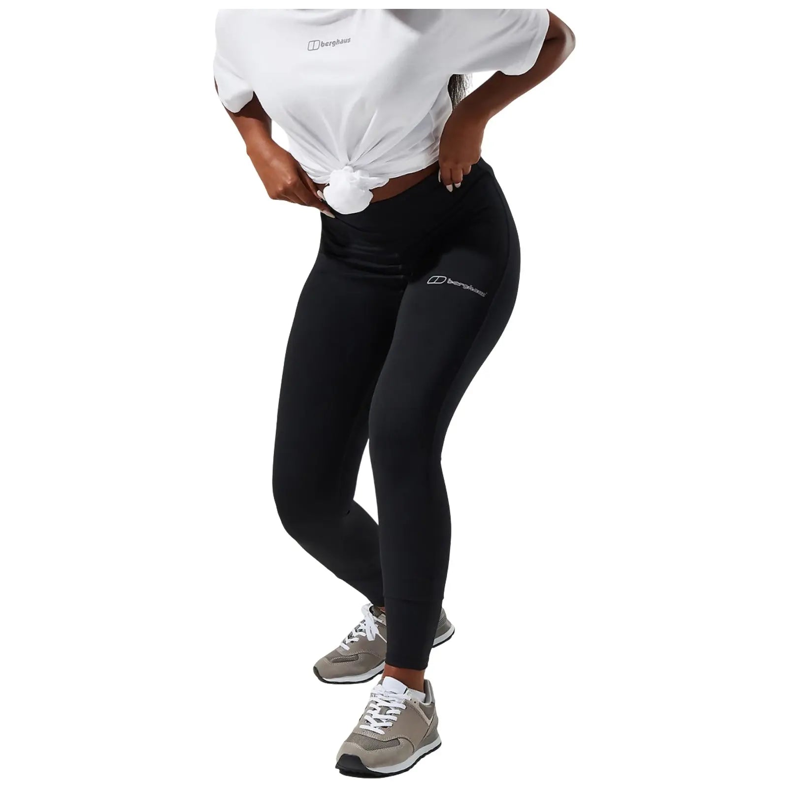 A person is wearing olive green leggings featuring a logo on the lower leg while standing with one hand resting on the hip and the other hand at their side.