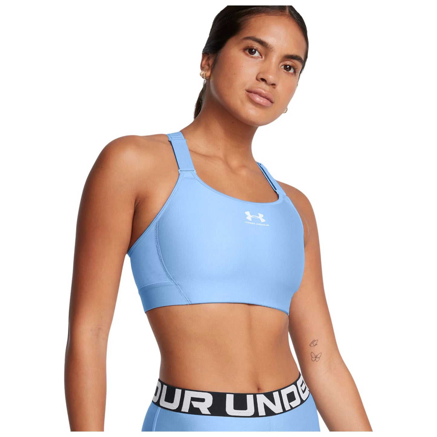 A young woman poses wearing a light blue fitted sports bra with a logo and matching high-waisted leggings featuring a bold waistband in a well-lit neutral background.