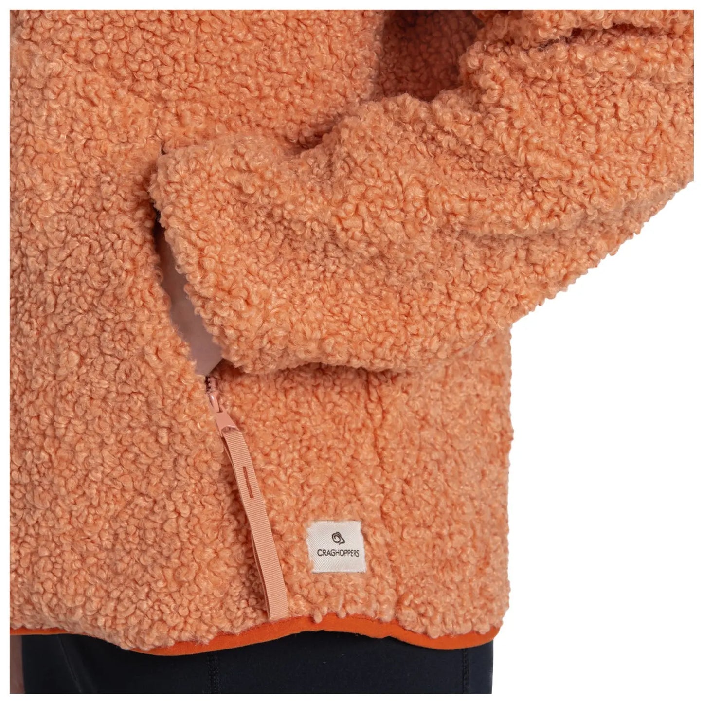 An orange fleece jacket with a textured surface features a side zip pocket and a visible brand label at the hem indicating Craghoppers, suggesting warmth and comfort in a casual setting.