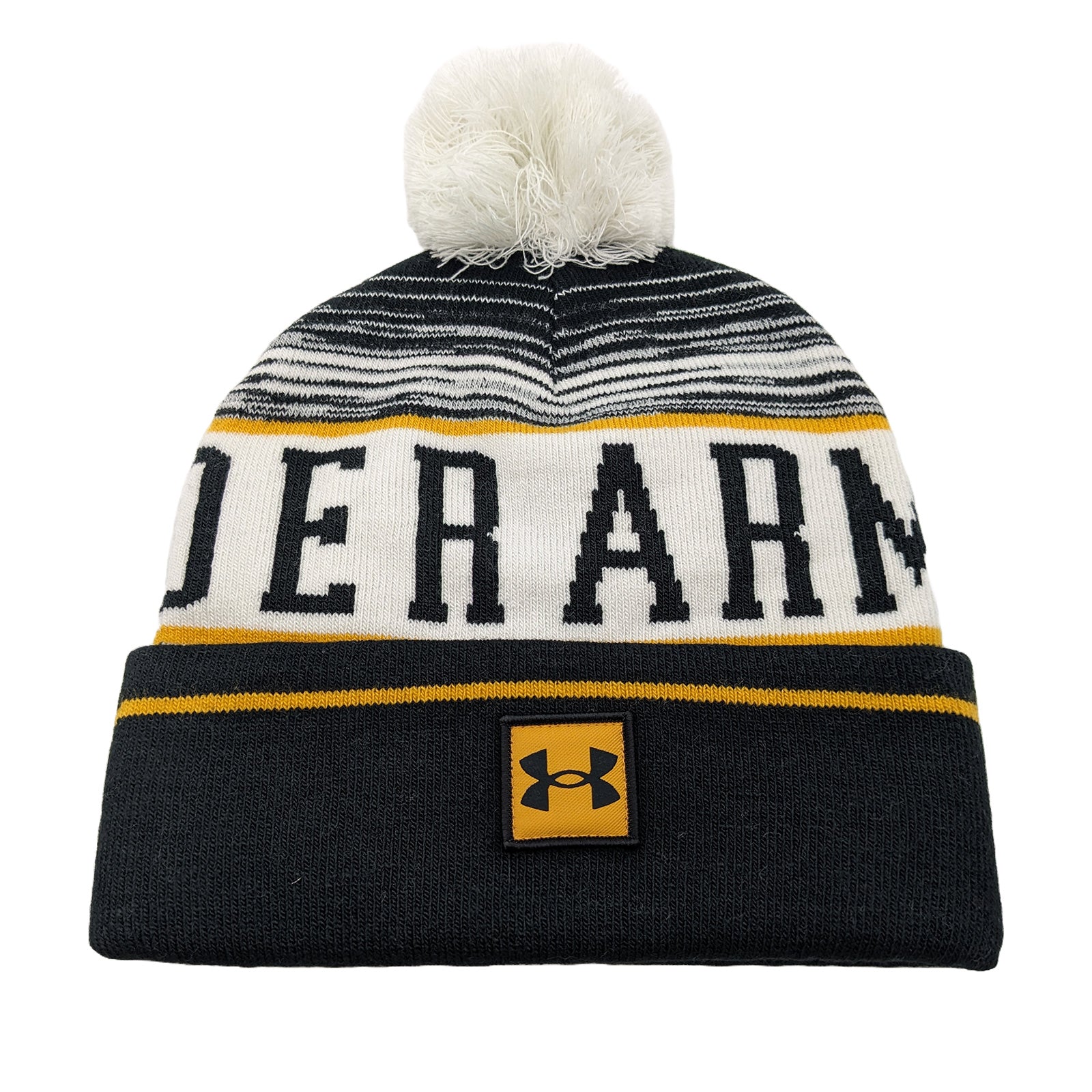 A knitted beanie with a white and black striped pattern features bold yellow and black letters spelling "UNDER ARMOUR" on the body and a logo patch sewn on the front. A fluffy pom-pom sits atop the hat.