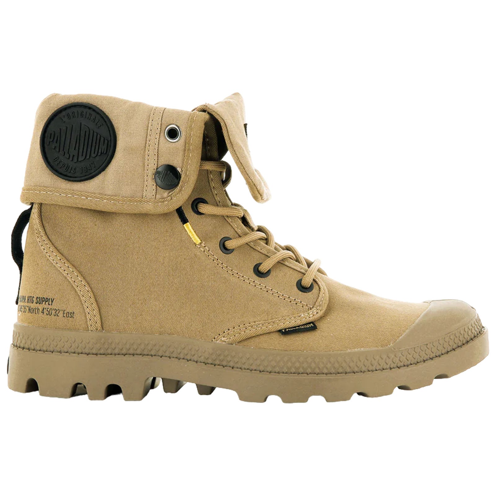 A tan canvas boot stands upright featuring metal eyelets and a foldable flap at the ankle with a circular logo tag the sole has a rugged tread design for traction.