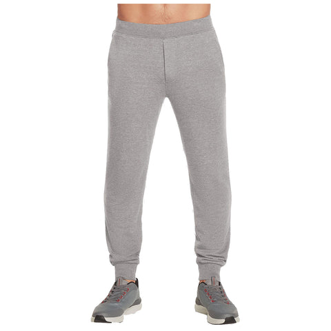 Gray sweatpants are worn by an individual standing upright with gray athletic shoes on their feet in a neutral setting. The individual’s torso is bare above the waistband.