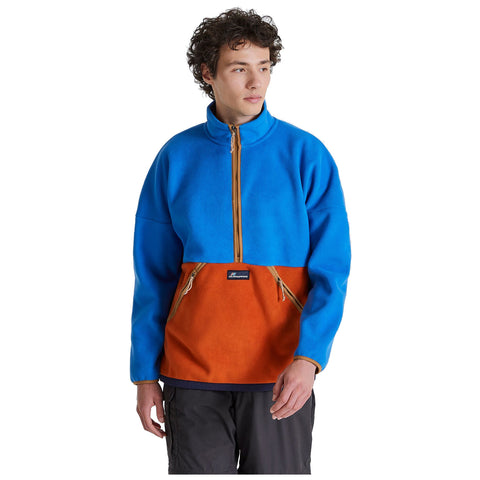 A young man is wearing a bright blue and orange fleece jacket with a half-zipper and front pockets while standing against a plain white background looking slightly to the side.