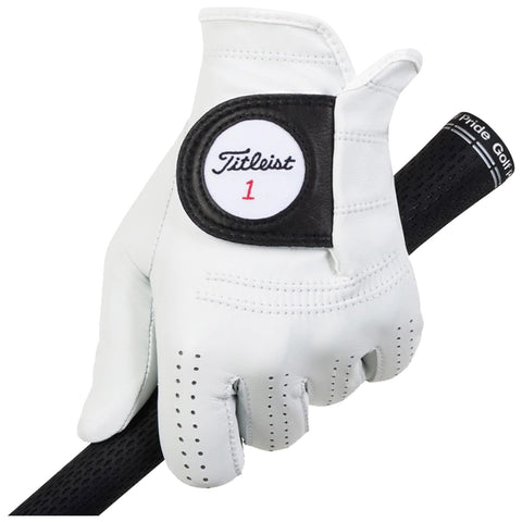 A white golf glove with a black label marked Titleist 1 grips the handle of a golf club while resting on a dark, textured surface suitable for golf.