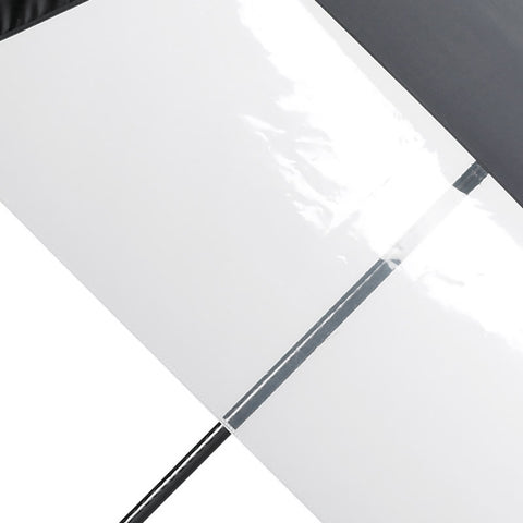 A black and white umbrella is positioned diagonally with its black canopy covering the top half and a translucent white panel on the bottom half in a neutral background.