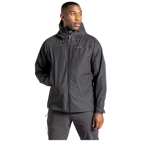 A man wears a hooded black jacket with a zipper and orange accents while standing in a neutral space, showcasing a relaxed but confident expression.