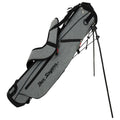 A golf bag is upright with a stand extended showcasing its gray fabric design and black accents featuring the brand name prominently displayed. It is positioned for easy access to golf clubs.