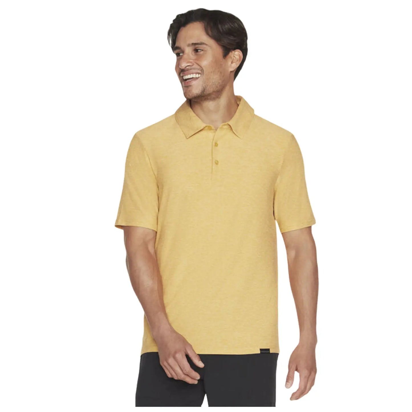 A smiling man wears a short-sleeved yellow polo shirt and stands with one hand raised slightly in a casual pose against a plain background.